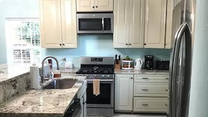 Una cocina con armarios de colores claros, un refrigerador de acero inoxidable, un microondas, una estufa y un lavaplatos.