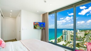 A bedroom with a large window offering a view of the sea and buildings. - 1902- Stunning sub-penthouse oceanview (Cupecoy)