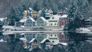 En rad färgglada hus vid en sjö, med snötäckta träd i bakgrunden.