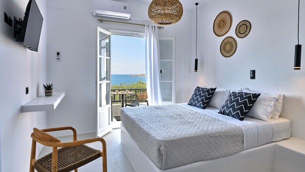 A bedroom with a bed, a chair, a TV, and a balcony with a view. - PAROS FIVE SENSES (Paros)