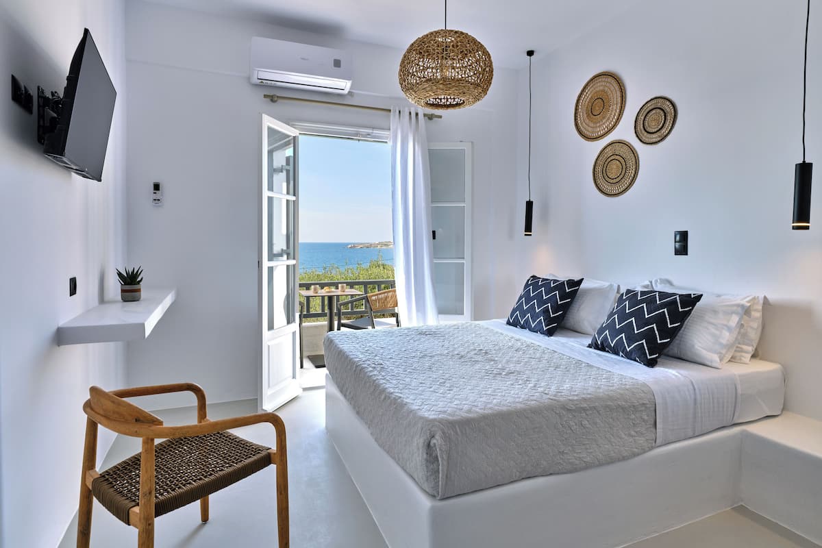 A bedroom with a bed, a chair, a TV, and a balcony with a view.