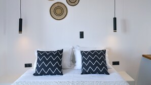A neatly arranged bedroom with a bed, two pillows, and three wall-mounted circular woven decorations. - PAROS FIVE SENSES (Paros)