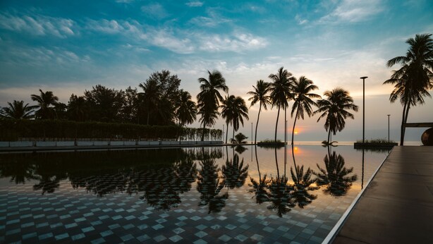 A reflective pool with palm trees and a sunset in the background. - The Bloc At Sea (Thap Sakae)