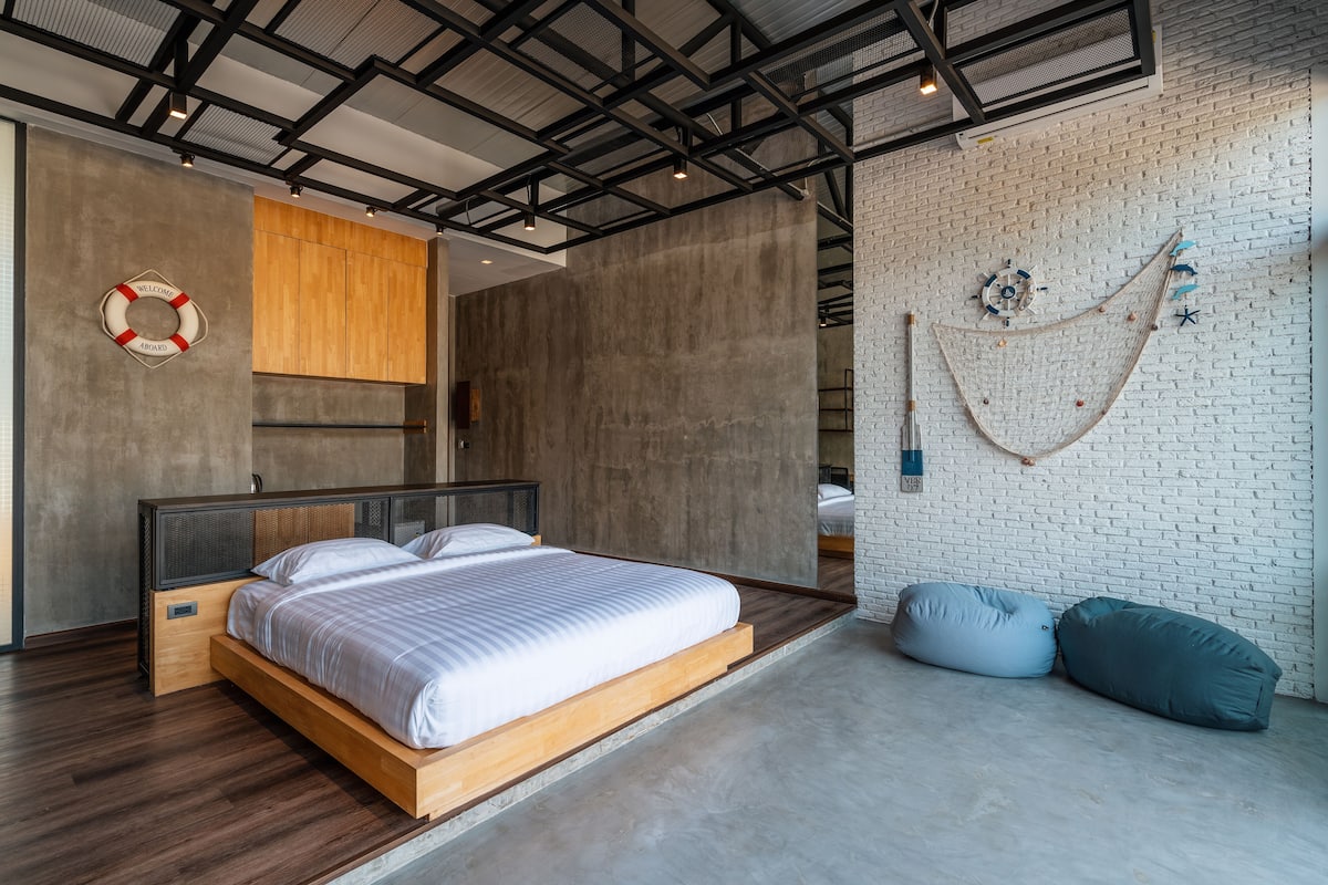 A modern bedroom with a wooden bed, a brick wall, and a ceiling with exposed beams.