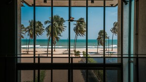 A view through a window with metal bars, featuring a beach with palm trees and the ocean. - The Bloc At Sea (Thap Sakae)