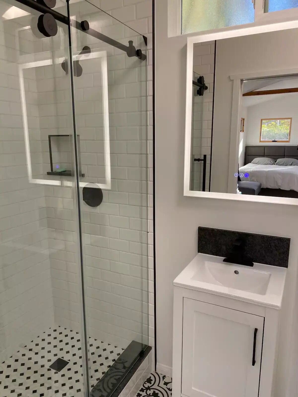 A modern bathroom with a glass shower enclosure, a white sink with a black countertop, and a mirror above the sink.