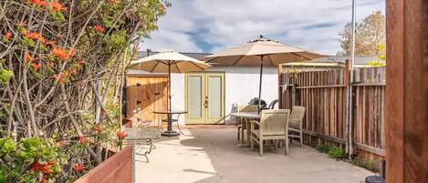 A backyard with a patio table and chairs, a wooden fence, and a tree with orange flowers.