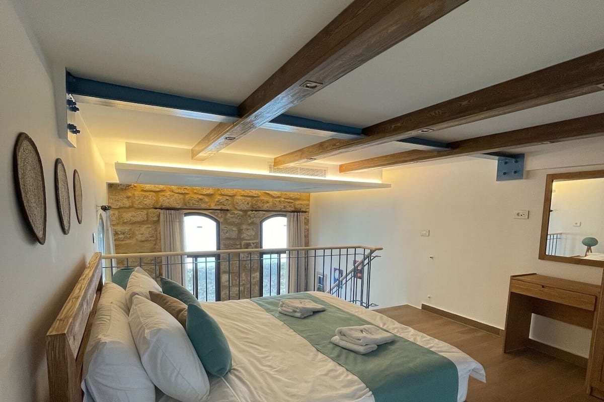 Un dormitorio con cama, un escritorio de madera, pared de piedra y balcón.