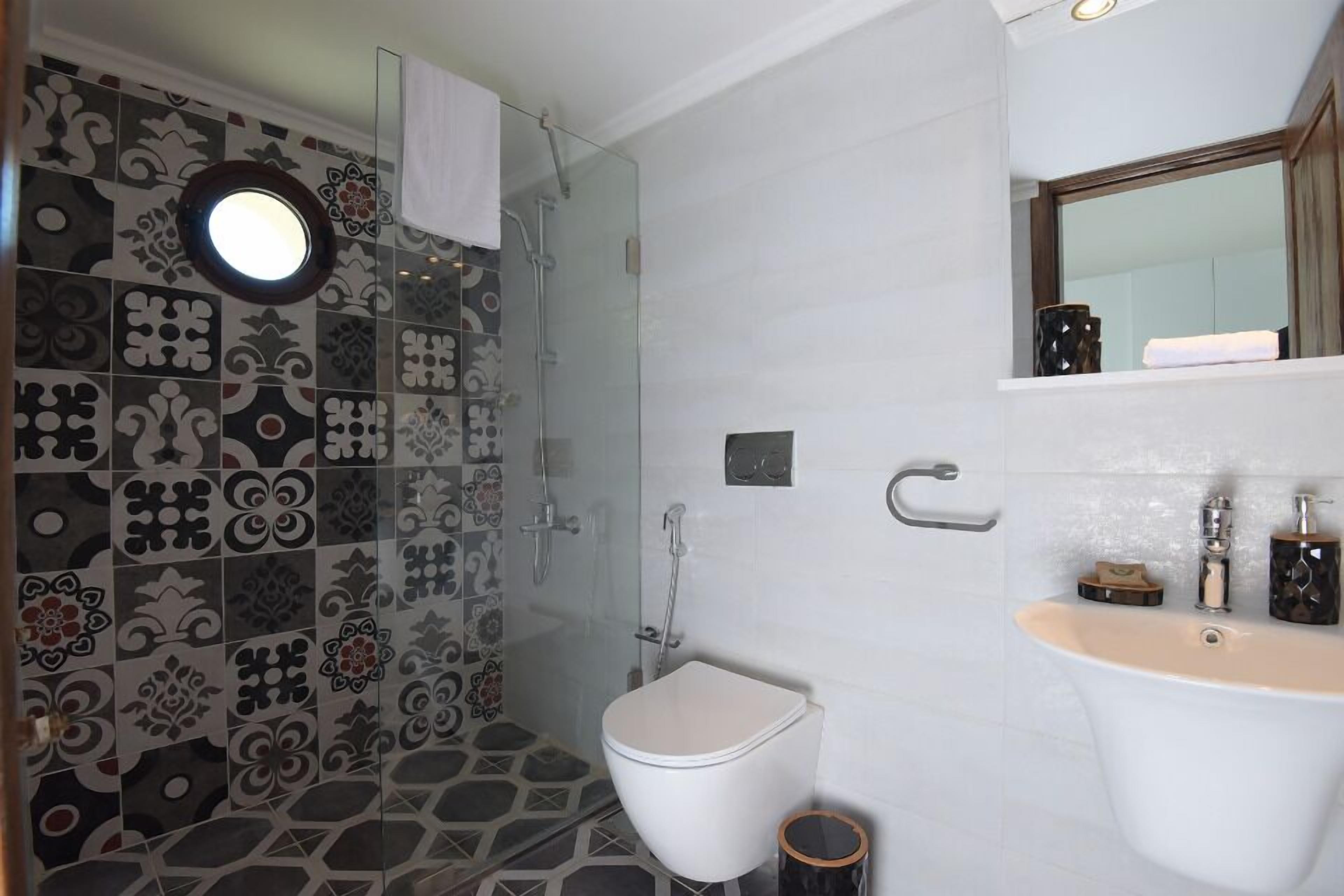 Une salle de bain avec des carreaux décorés, des toilettes, une douche et un lavabo équipé de produits de toilette.