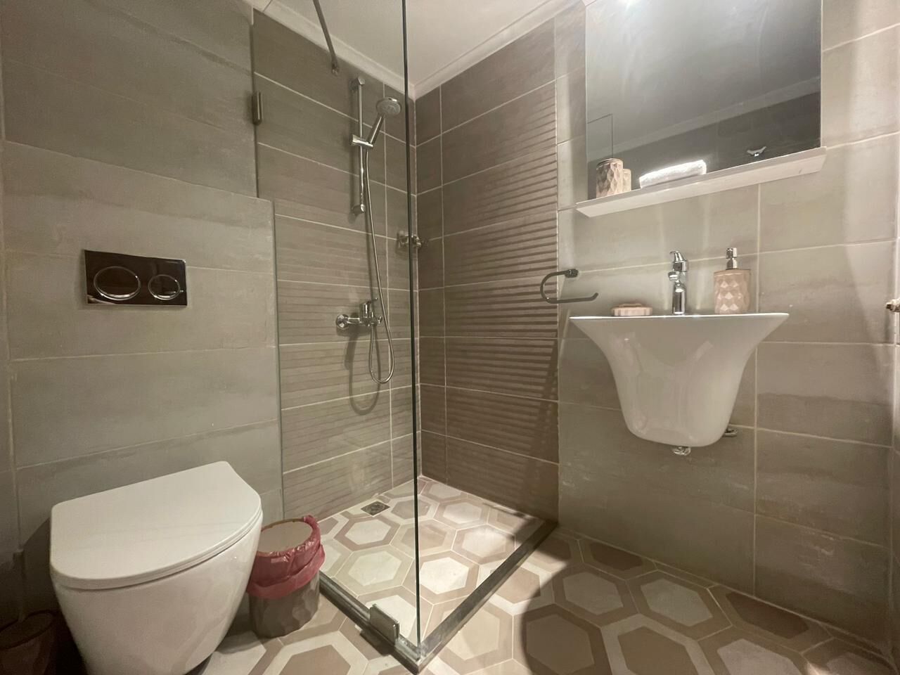 Une salle de bain avec une douche à parois de verre, des toilettes et un lavabo avec un miroir au-dessus.