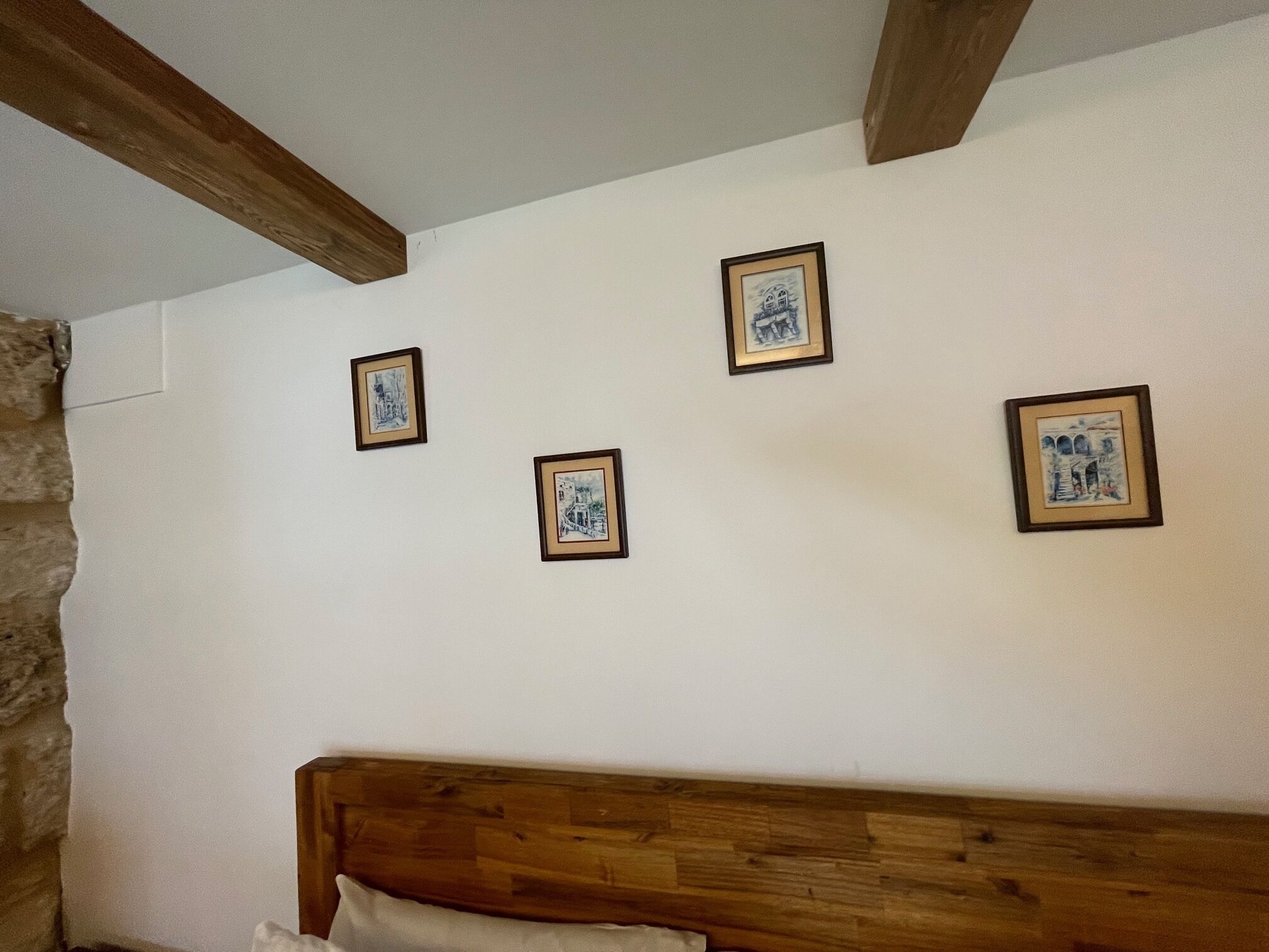 Un dormitorio con cabecera de madera, pared de piedra y tres cuadros en la pared.