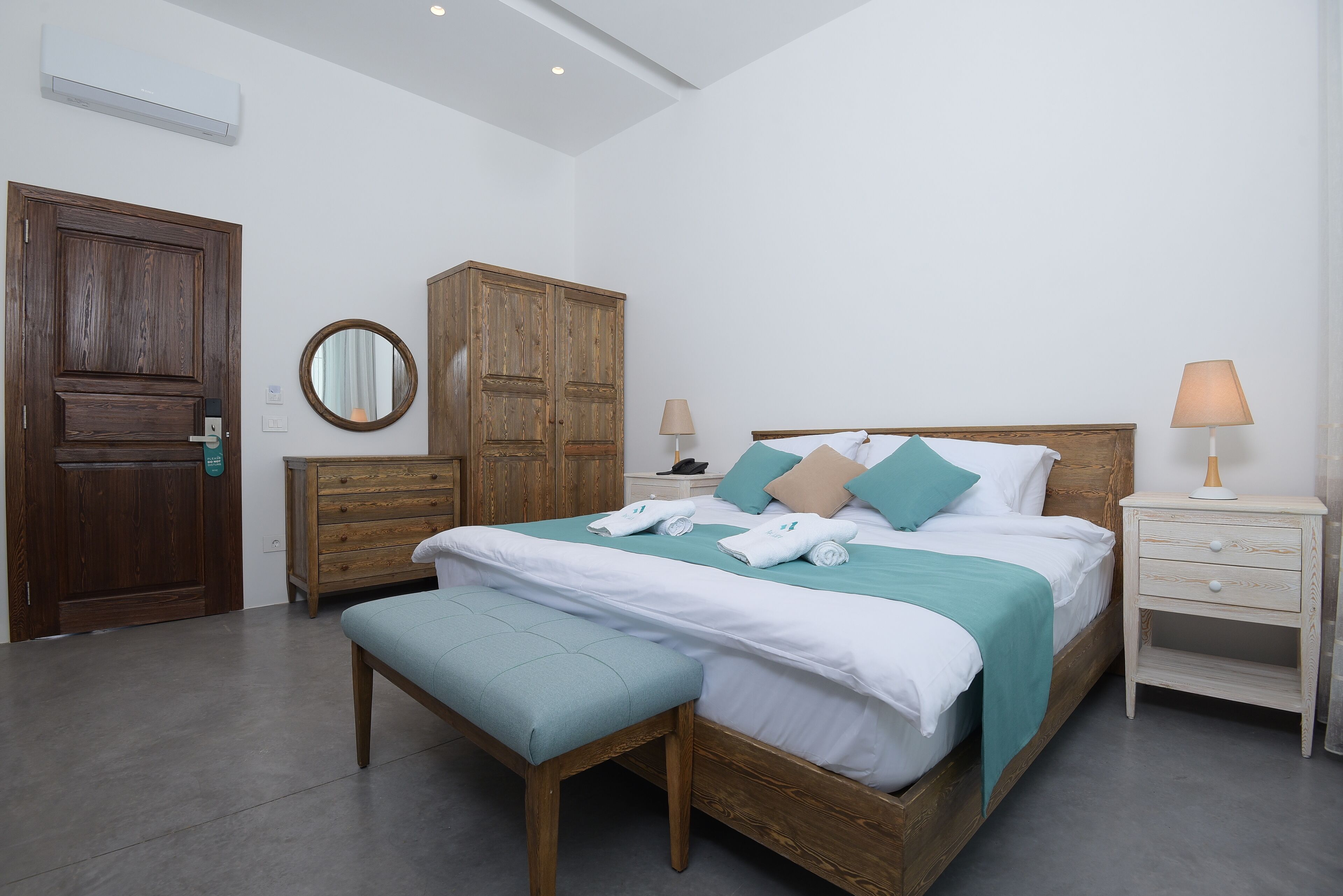 Een slaapkamer met een houten bed, een bankje, een kledingkast, twee nachtkastjes en een spiegel.