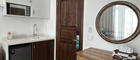 A compact kitchen with a microwave, a refrigerator, a wooden door, and a mirror.