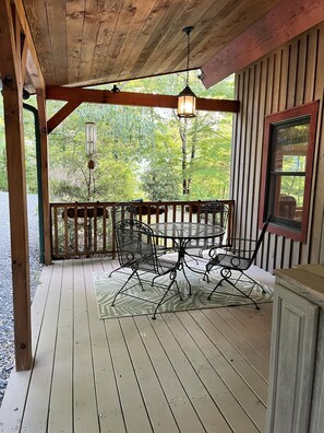 Un terrazzo in legno con tavolo e sedie, un lanterne appesa e una finestra vista alberi.