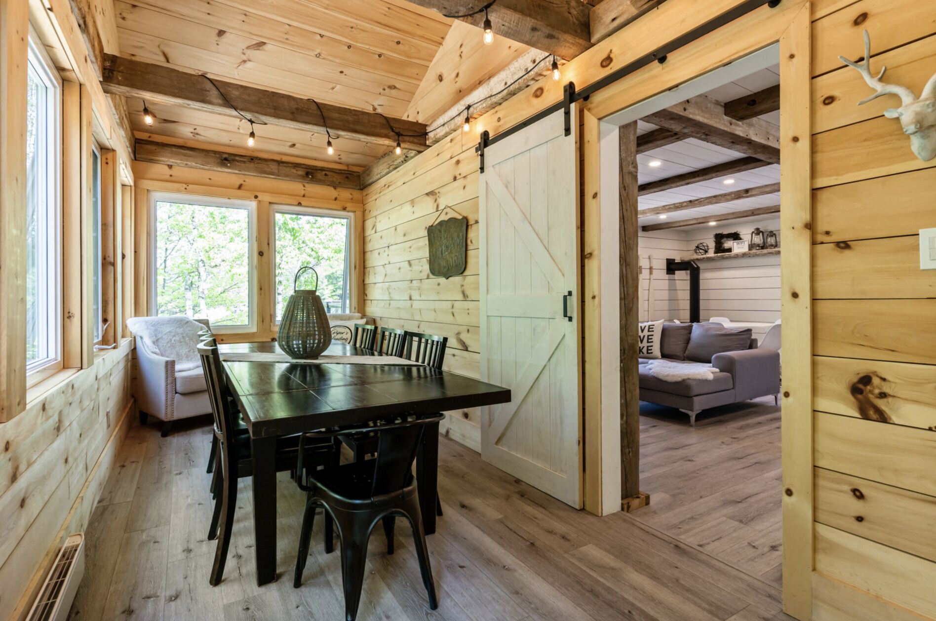 A wooden interior with a dining table, chairs, a sofa, and a sliding barn door.