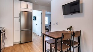 A modern kitchen with a stainless steel refrigerator, a wooden dining table with chairs, and a mounted flat-screen TV on the wall. - Modern Seattle Townhome Near Downtown & Parks (Seattle)