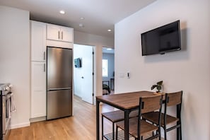 A modern kitchen with a stainless steel refrigerator, a wooden dining table with chairs, and a mounted flat-screen TV on the wall. - Modern Seattle Townhome Near Downtown & Parks (Seattle)