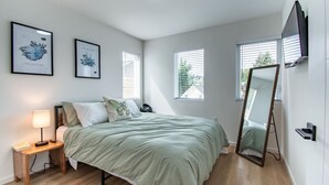 A bedroom with a bed, bedside table, lamp, framed artwork, windows, and a mirror. - Modern Seattle Townhome Near Downtown & Parks (Seattle)