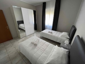 A hotel room with two beds, a wardrobe, a mirror, and a window with curtains.