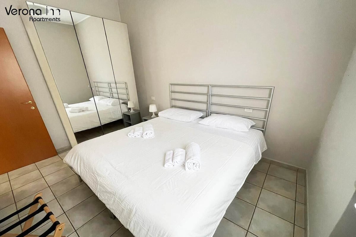 Ein Hotelzimmer mit einem großen Bett, einem Kleiderschrank, einem Spiegel und einem Holzsessel.