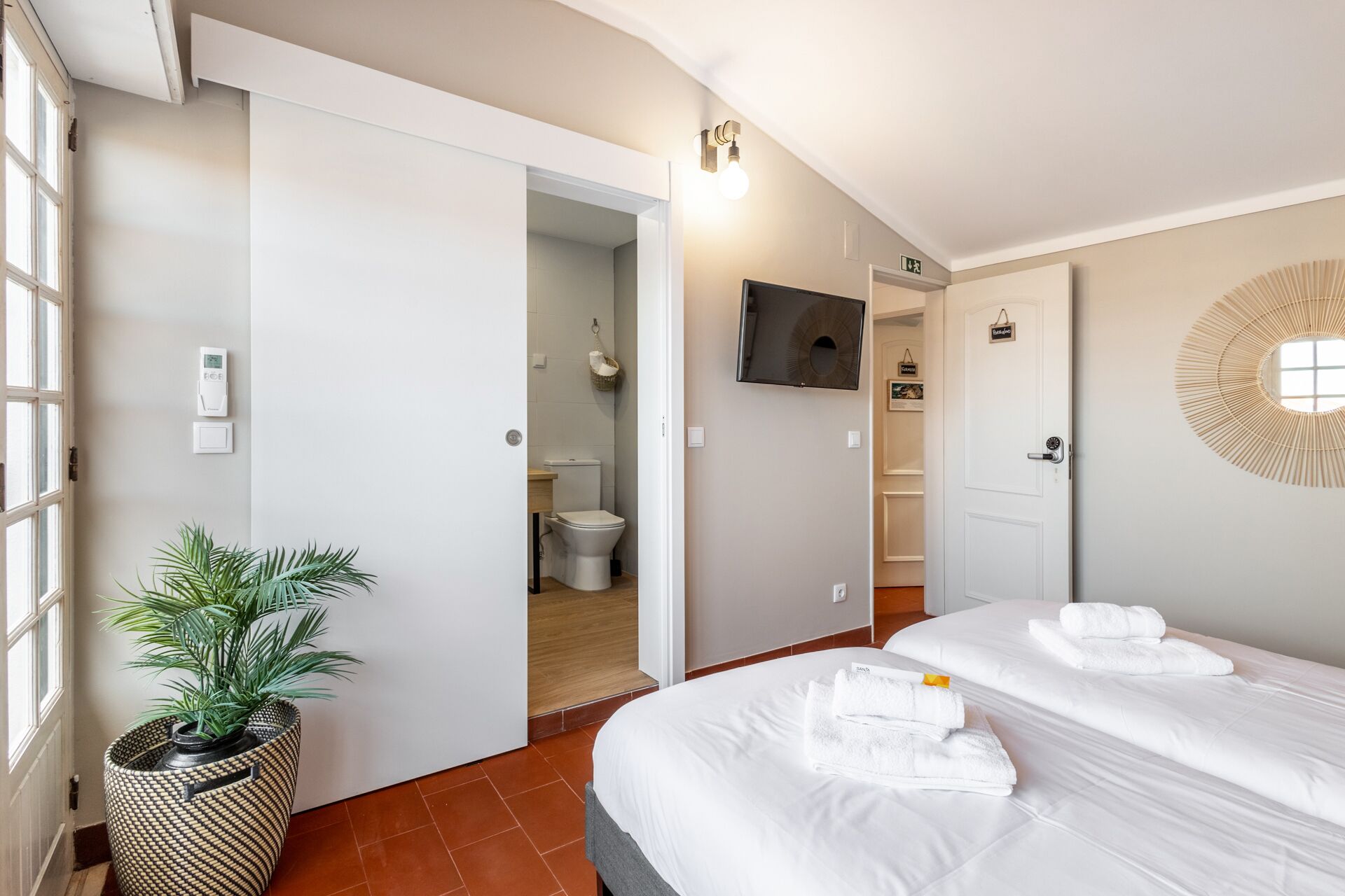 Quarto de hotel com cama, televisão, banheiro e planta em vaso.