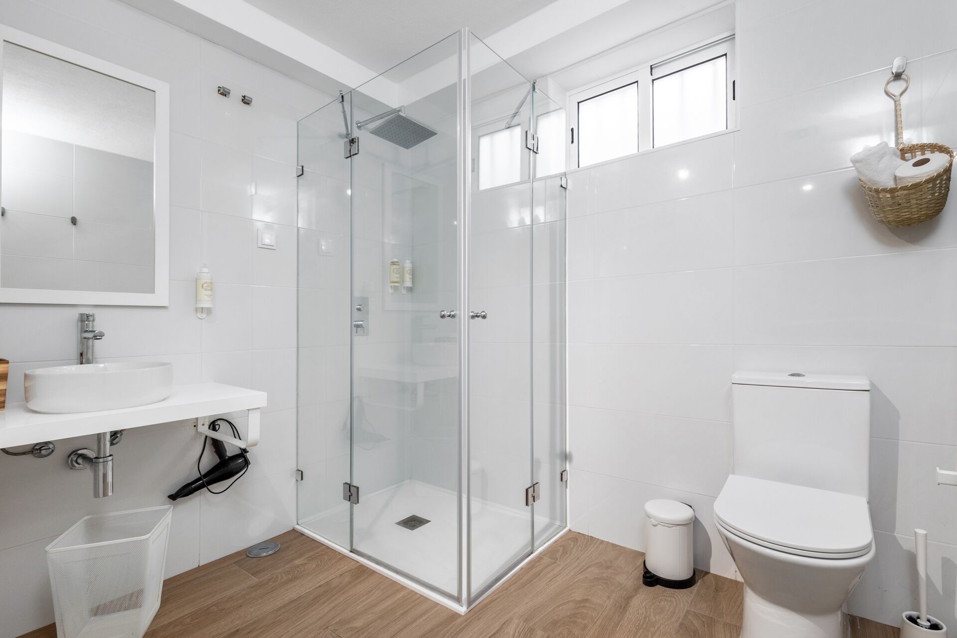Un baño moderno con ducha de vidrio, inodoro y lavamanos con espejo.