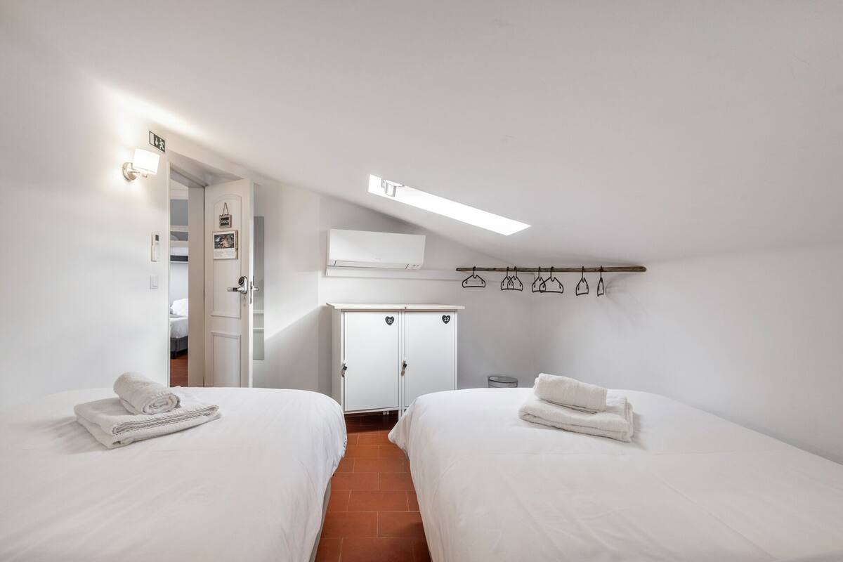 A bedroom with two beds, a wardrobe, a coat rack, and a small table.