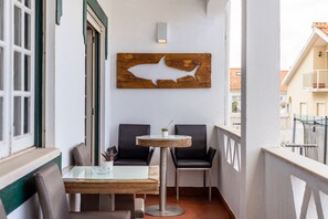 A balcony with a table and chairs, a wooden wall art piece, and a view of the cityscape. - Santa Sea & Sun (Torres Vedras)