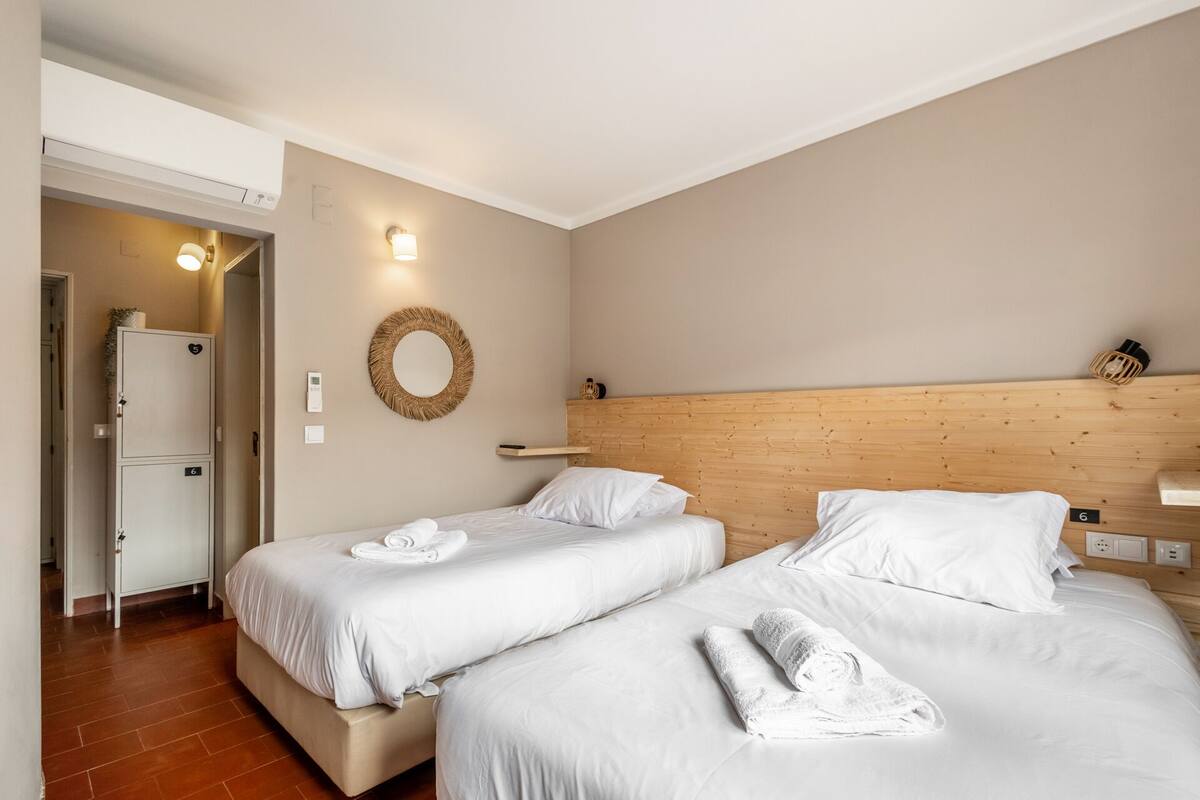 A hotel room with two beds, a wooden headboard, a wall-mounted mirror, and a door with a number sign.