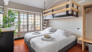 Une chambre avec un lit, un lit mezzanine en bois, une plante, une fenêtre et une porte.