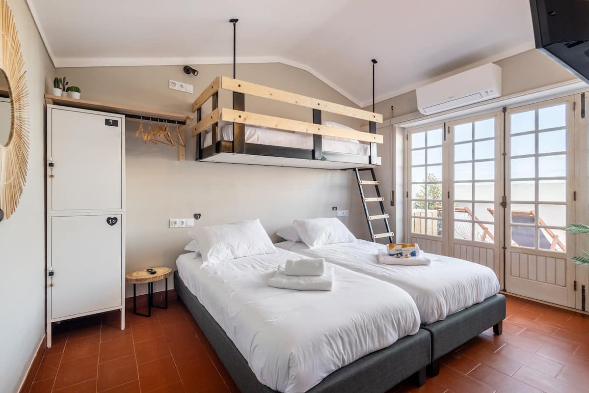A bedroom with two beds, a wardrobe, a vanity, and a window with a view.
