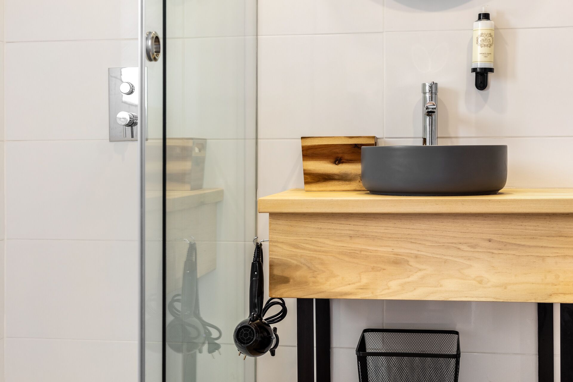 Un baño con cabina de ducha de vidrio, tocador de madera con lavamanos negro y un secador de pelo negro sobre la encimera.