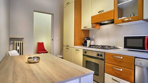 Ett kompakt kök med ett träbord, en röd stol, en spis, en ugn, en mikrovågsugn och en diskmaskin.
