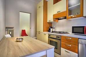 A compact kitchen with a wooden table, a red chair, a stove, an oven, a microwave, and a dishwasher. - Suite Mery (Verona)