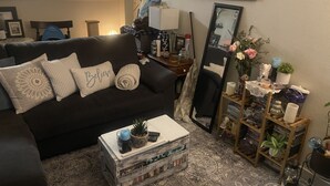 En hyggelig stue med en mørk sofa, et sofabord med bøger, et spejl og en lille reol.
