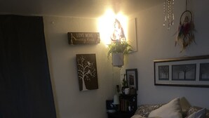Et soveværelse med en seng, puder, et tæppe, et natbord med en lampe, en væg med et skilt og en drømmefanger.