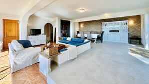 A spacious living area with a sofa, a television, and a kitchen area in the background. - Cardina CostaBravaSi - Pool, A/C, barbecue, views (Sant Feliu de Guíxols)