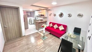 Una sala de estar moderna con un sofá rojo, una mesa de centro de vidrio y una cocina al fondo.