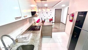Una cocina moderna con encimera de granito, pileta de acero inoxidable y horno empotrado. Hay una zona de comedor con una mesa y sillas, y un refrigerador a la derecha.