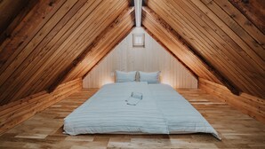 An attic bedroom with wooden slats on the ceiling, a bed with a striped blanket, and a small window at the end of the room.