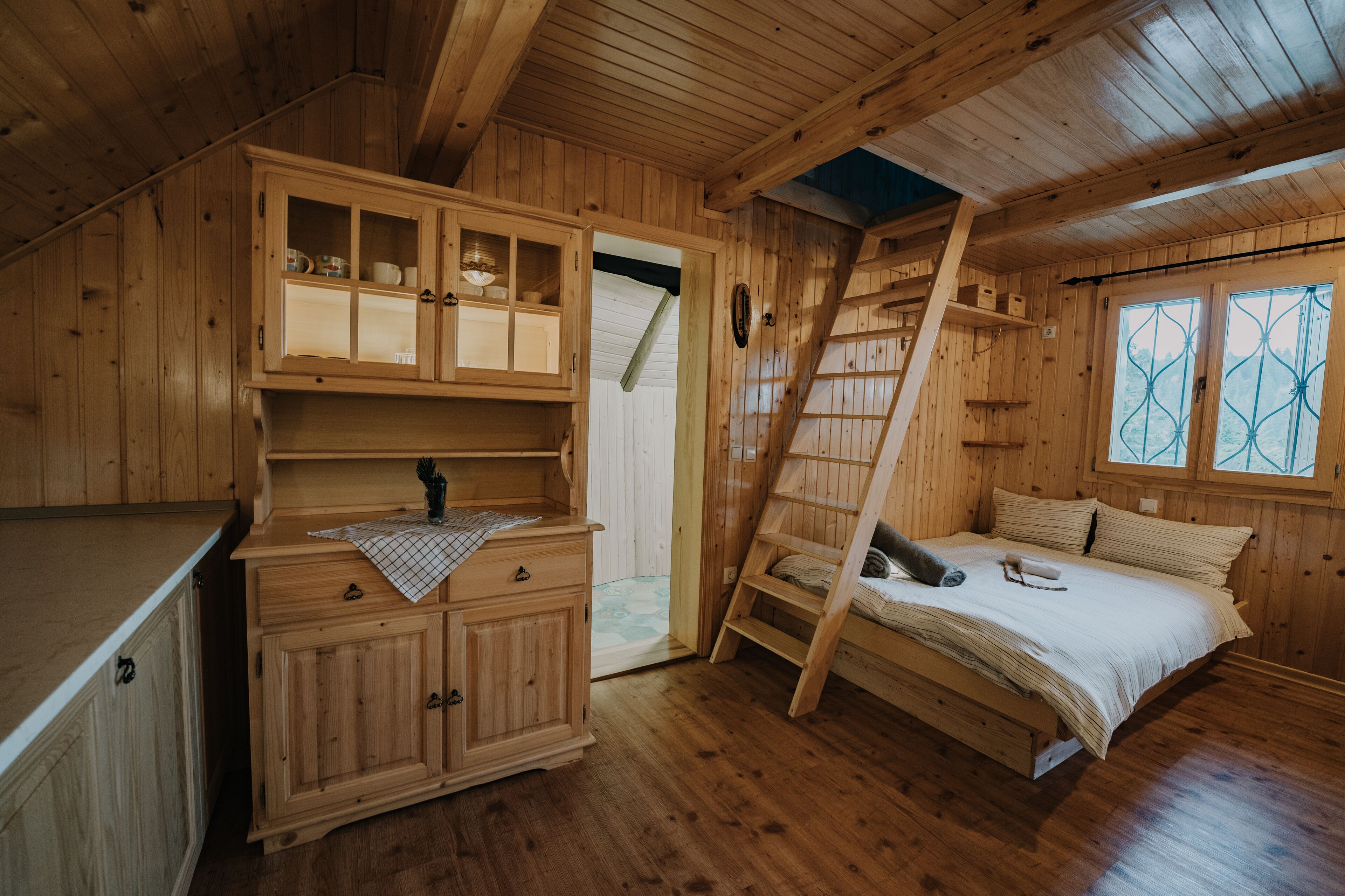 A wooden cabin with a loft bed, a small kitchenette, and a window with decorative glass.