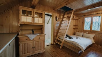 A wooden cabin with a loft bed, a small kitchenette, and a window with decorative glass.