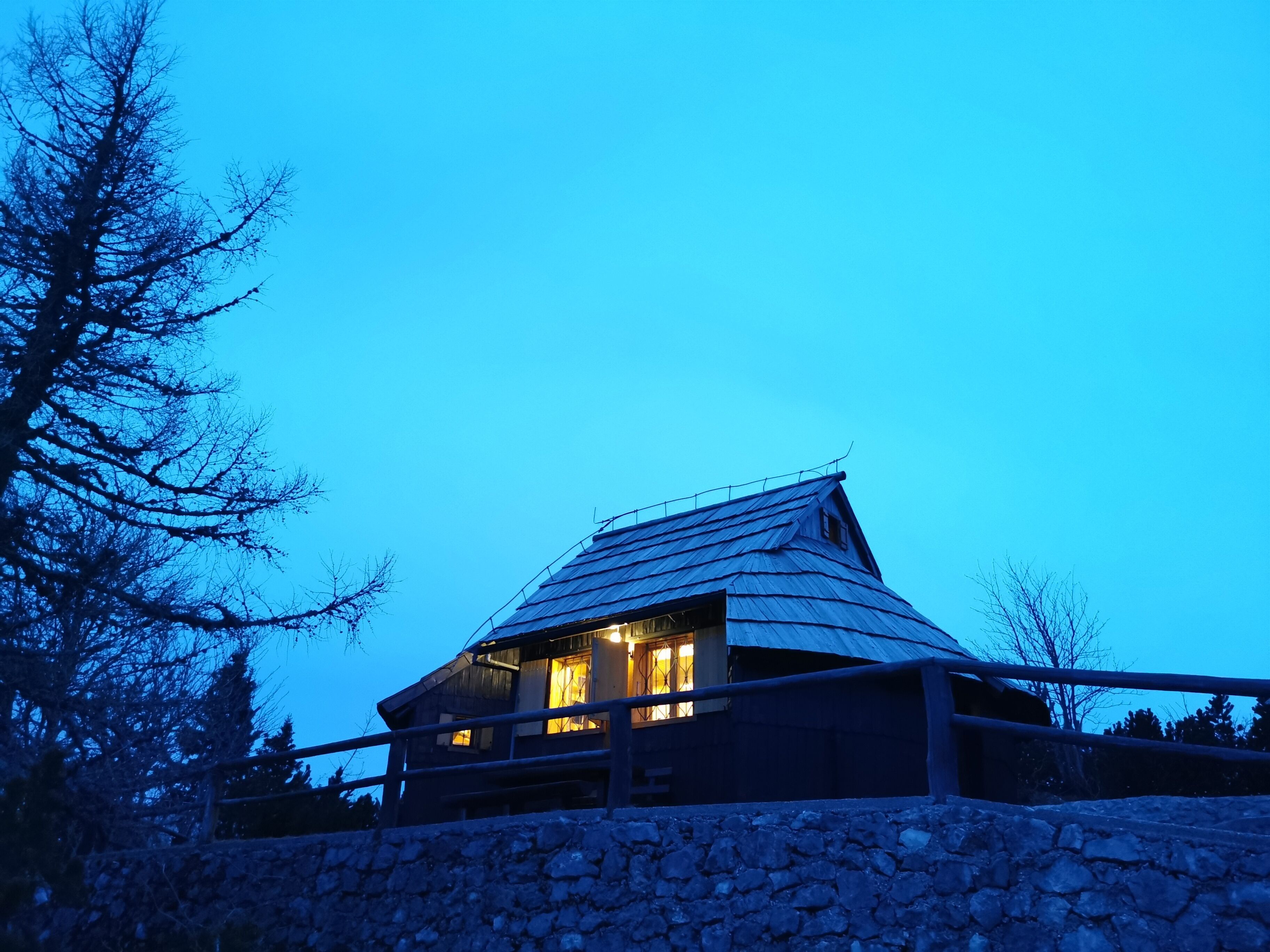A stone-walled building with a sloped roof and a metal railing in front.