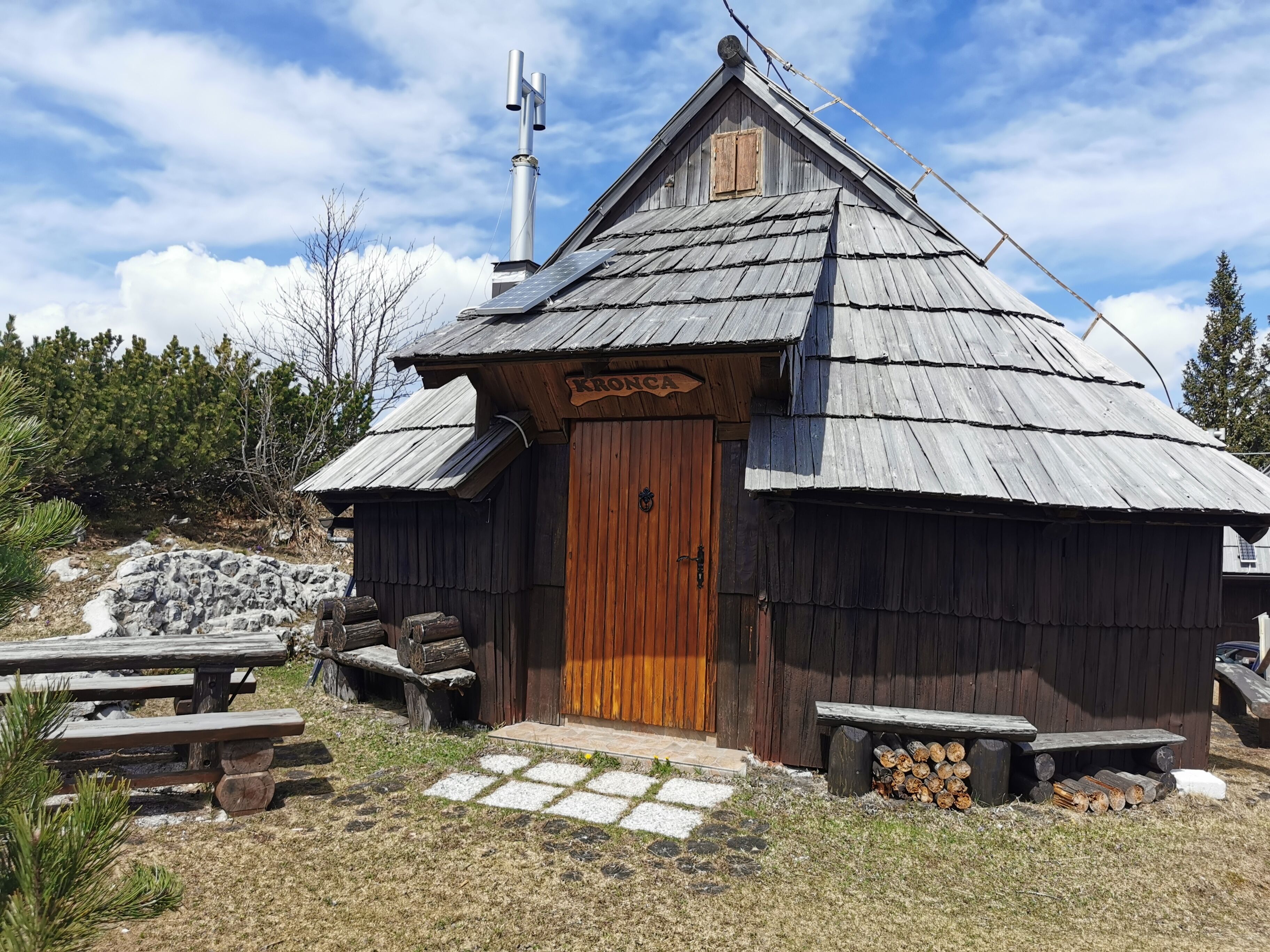 Une cabane rustique en bois, avec une porte en bois, une enseigne au-dessus de la porte et un petit porche doté de bancs.