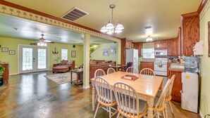 A spacious living area with a wooden dining table, chairs, and a sofa. There is a kitchen with wooden cabinets and appliances. - Spacious Lake Texoma Vacation Rental w/ Game Room! (Kingston)