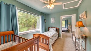 A bedroom with a bed, a wooden crib, a ceiling fan, a window with curtains, and a mirror with a lamp. - Spacious Lake Texoma Vacation Rental w/ Game Room! (Kingston)