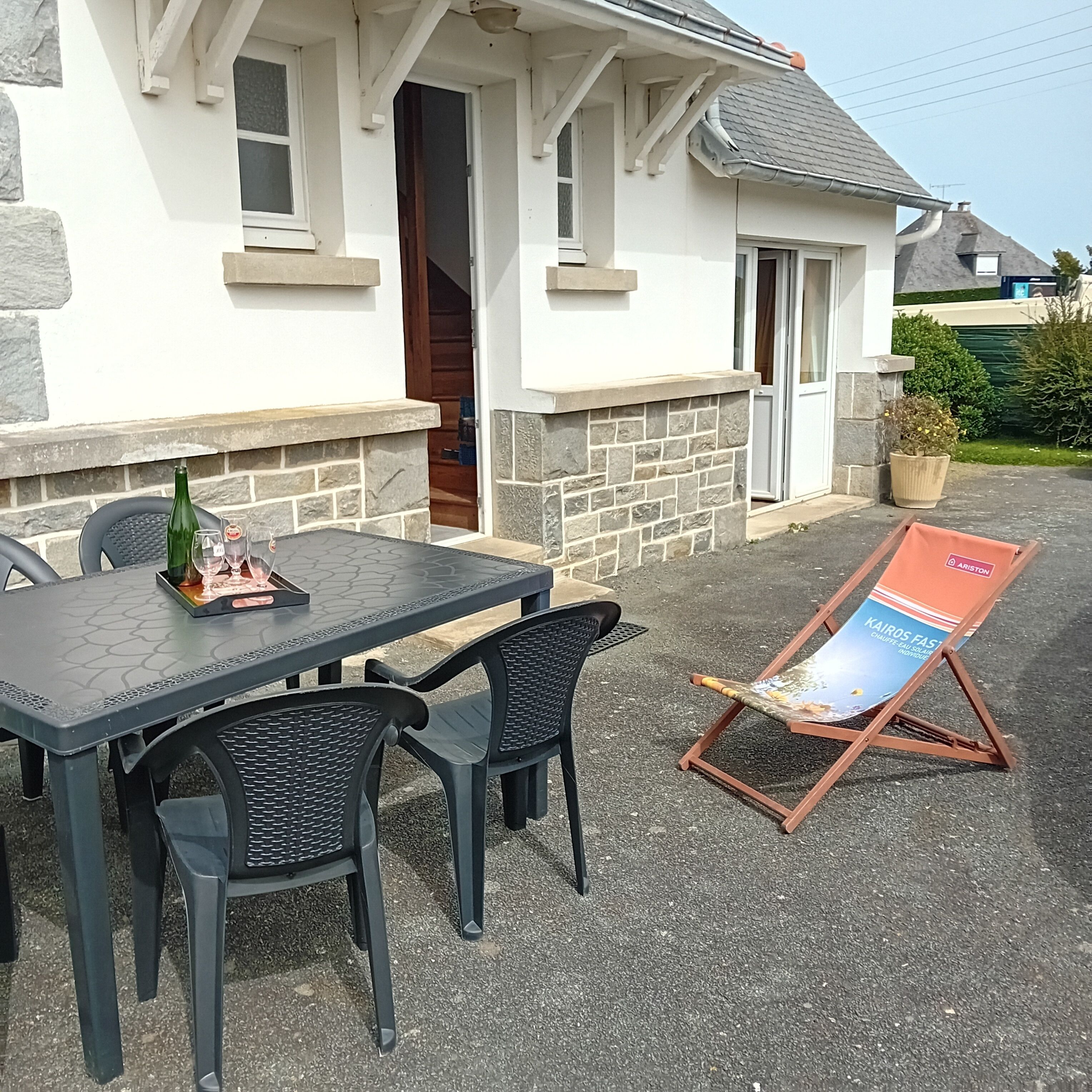 A patio with a table and chairs, a bottle, and glasses, and a signboard outside a building.
