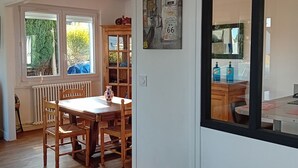 A dining area with a wooden table and chairs, a radiator, and a window with a view of greenery.