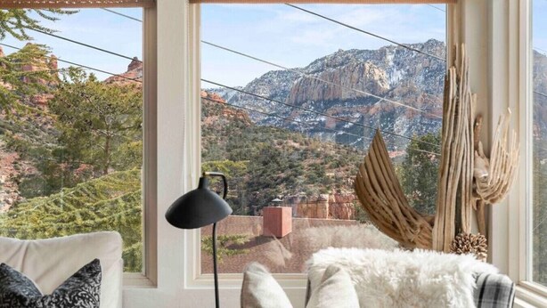 Habitación acogedora con un amplio ventanal que ofrece vistas a la montaña, una lámpara de escritorio negra y un mullido almohadón blanco.