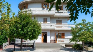 Un edificio de varios pisos con fachada curva, balcones con persianas de madera y una entrada central con escalones.